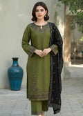 Woman wearing a green embroidered outfit with a black dupatta in an outdoor setting.
