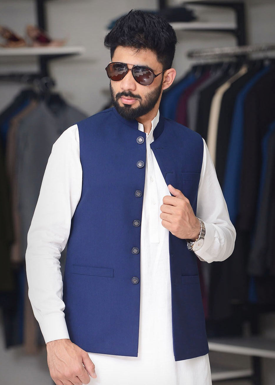 Man wearing a blue vest over a white shirt with sunglasses, standing in a clothing store.