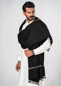 Man wearing a black scarf with gold trim over a white outfit on a light gray background