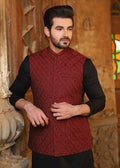 Man wearing a red patterned vest over a black shirt in an indoor setting with wooden walls and stained glass.
